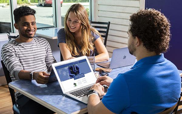 三名学生围坐在一张桌子旁，用笔记本电脑访问UWF网站.